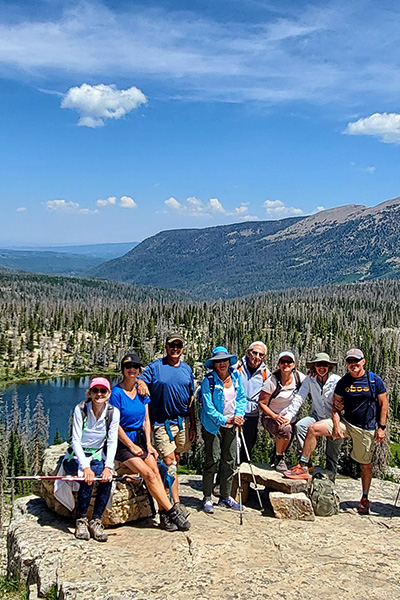 Red Ledges members smiling at the summit during a group hiking event, surrounded by panoramic mountain views.