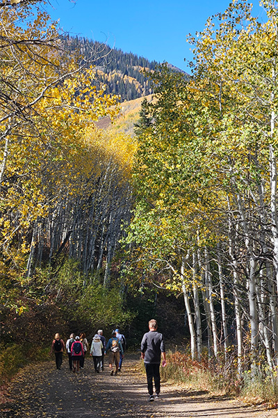 Members hiking a forested trail during fall, with colorful leaves scattered on the ground near Red Ledges.